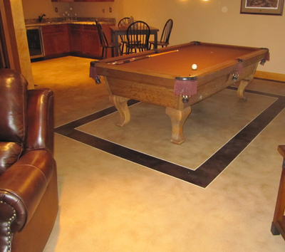 Textured concrete floor in the basement of a home with a pool table over a square detail.