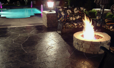 Stamped concrete patio with built in fire pit next to an in ground pool.